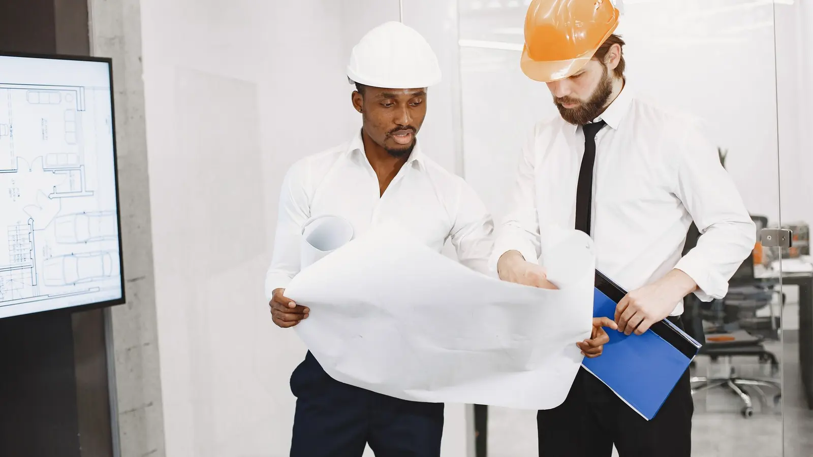 Two engineers in hard hats reviewing a large drawing together